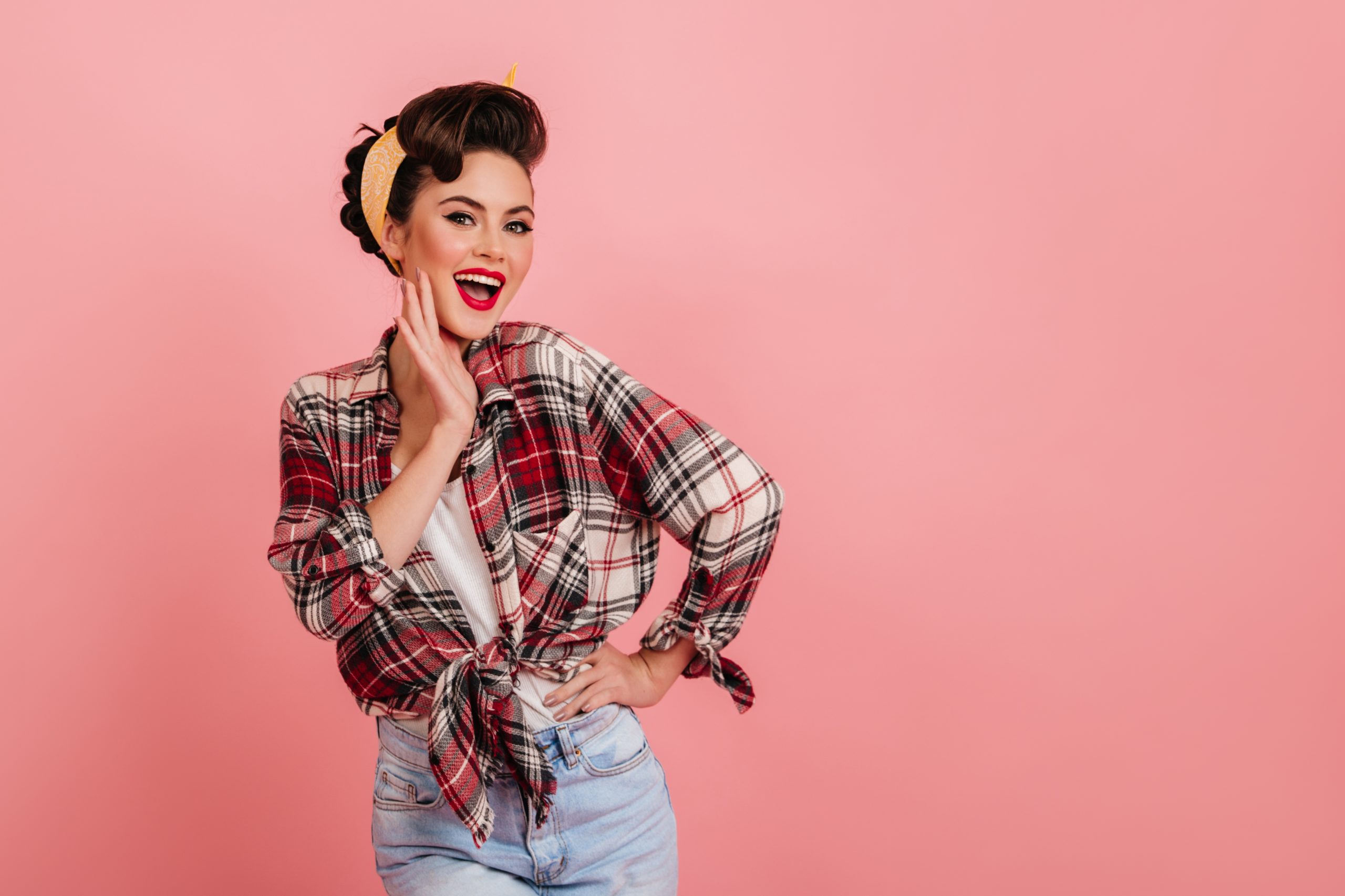Smiling gorgeous girl in checkered shirt posing on pink background. Studio shot of good-looking pinup woman